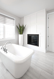 Salle de bain avec des murs gris clair devenant blanc, ton sur ton, avec un motif carré fait de planches mettant en lumière un foyer.